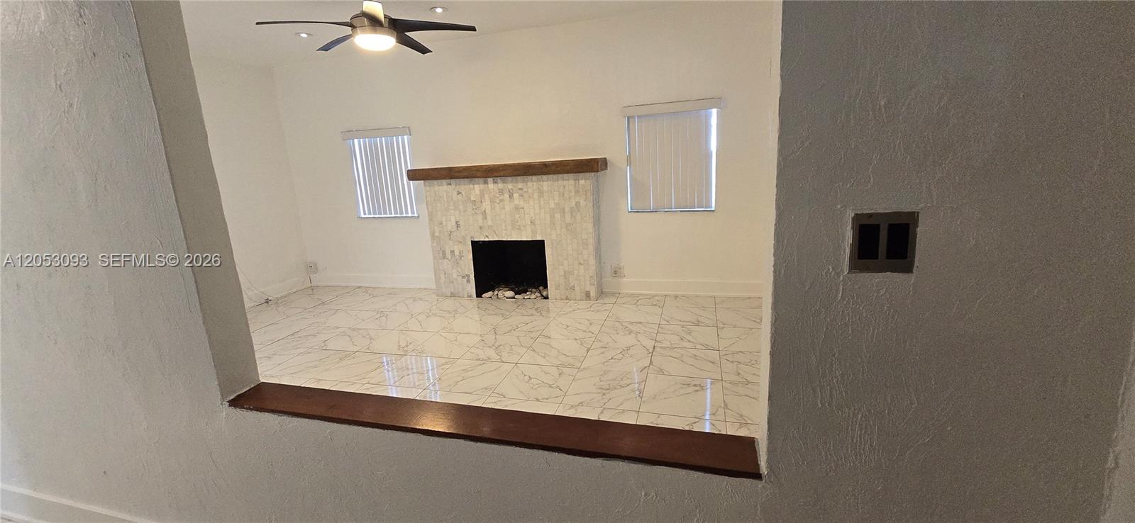 A living room features a tiled fireplace, marble-patterned floors, and a ceiling fan — 455 NE 131st St # 1, North Miami FL 33161, NORTH MIAMI, FL