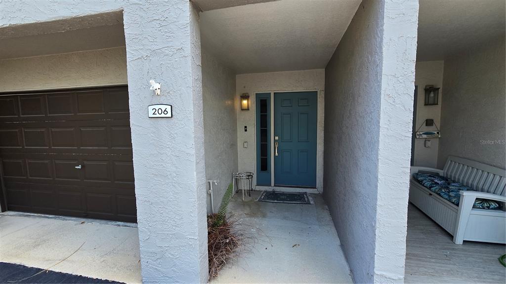 The exterior entrance features a blue front door, a garage, and a white bench — 521 PINELLAS BAYWAY S UNIT 206, TIERRA VERDE, FL