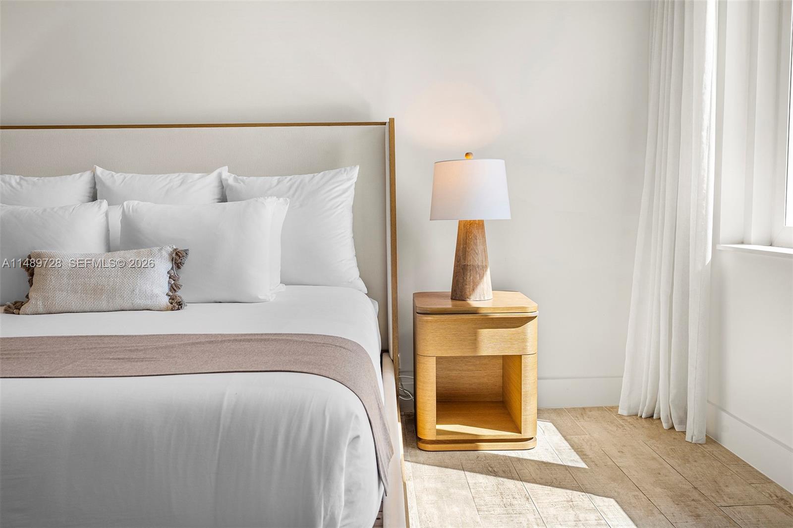 A bedroom features a bed with white linens, a wooden nightstand, and a table lamp — 102 24th St # 1412, Miami Beach FL 33139, MIAMI BEACH, FL