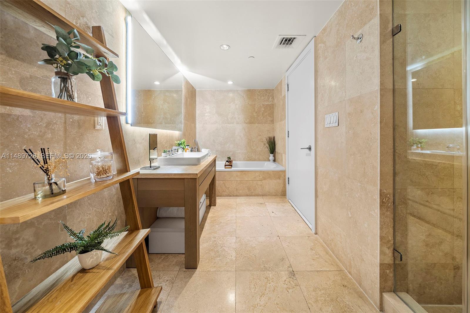 A modern bathroom features beige stone tile walls and floors, a wooden vanity, and a tub — 102 24th St # 1412, Miami Beach FL 33139, MIAMI BEACH, FL