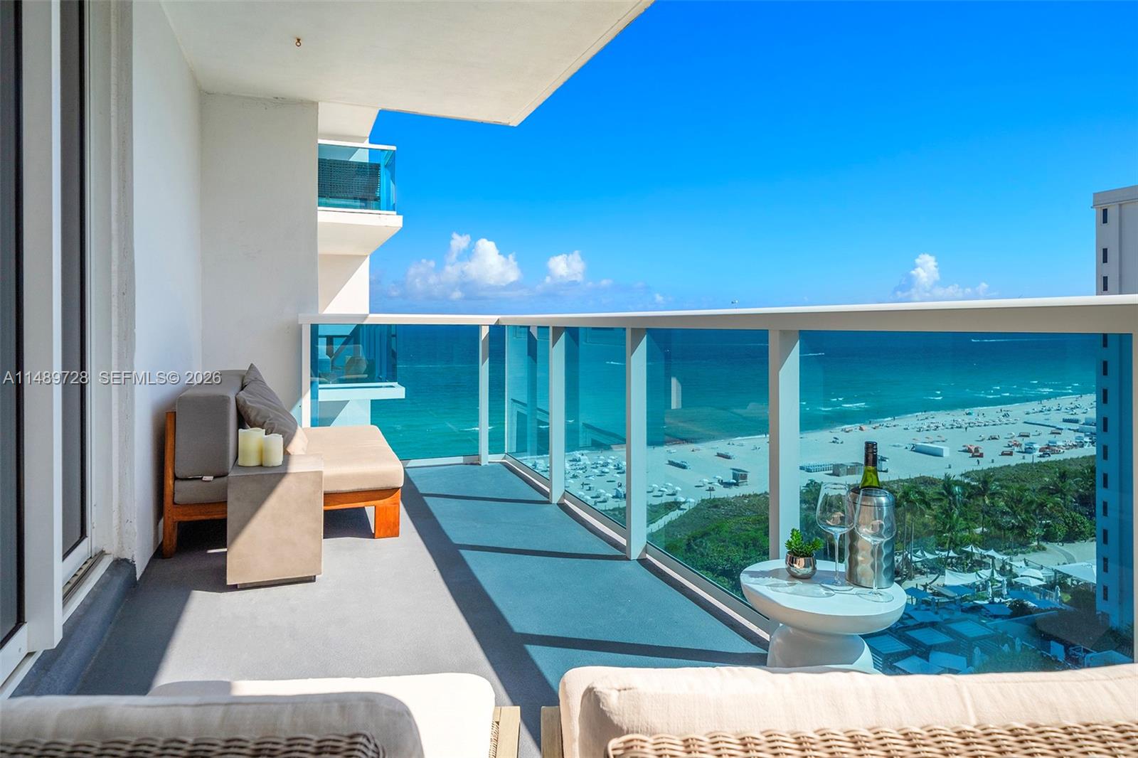 A balcony with outdoor seating overlooks a beach and the ocean under a clear sky — 102 24th St # 1412, Miami Beach FL 33139, MIAMI BEACH, FL
