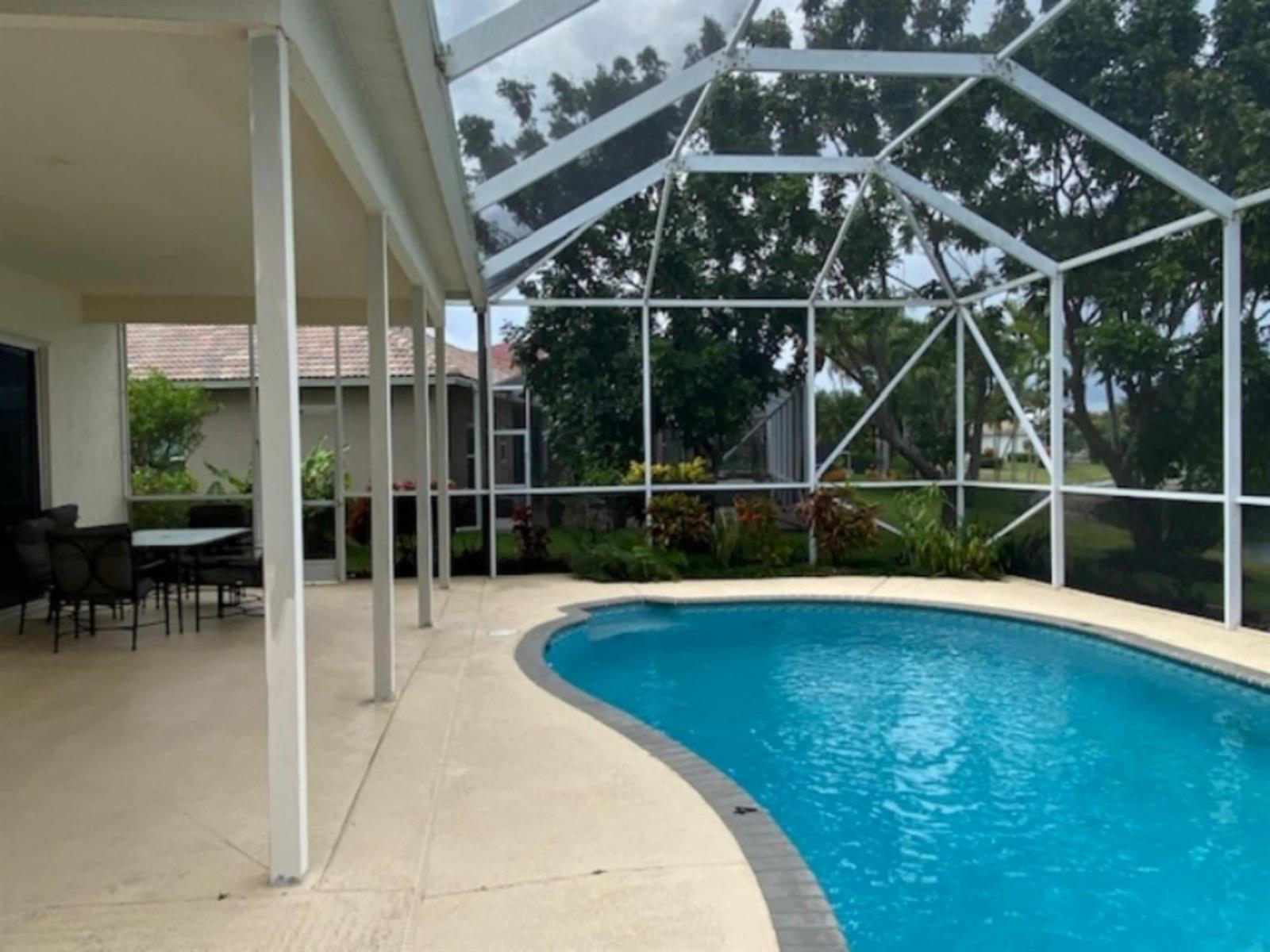 A screened-in patio features a curved swimming pool and a covered outdoor dining area — 18756 Cape Sable Drive, Boca Raton FL 33498, BOCA RATON, FL