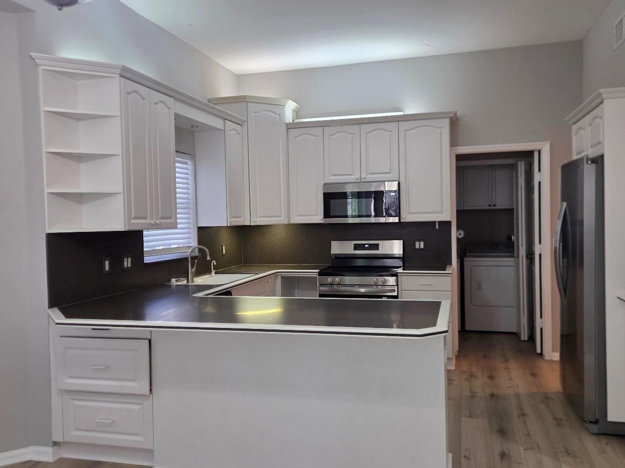 A kitchen features white cabinets, dark countertops, stainless steel appliances, and light wood-look flooring — 18756 Cape Sable Drive, Boca Raton FL 33498, BOCA RATON, FL