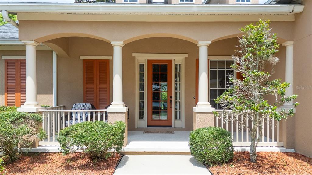 A covered front porch features a terracotta-colored door, white columns, and a wooden railing — 314 W LAKE VICTORIA CIRCLE, DELAND, FL