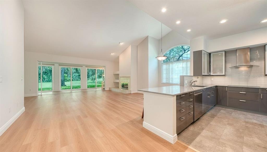 A modern kitchen with gray cabinets and a light-filled living area with sliding glass doors — 4004 PENSHURST PARK, SARASOTA, FL