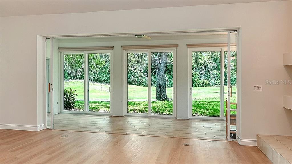 A room with light wood flooring features large sliding glass doors opening to a backyard — 4004 PENSHURST PARK, SARASOTA, FL