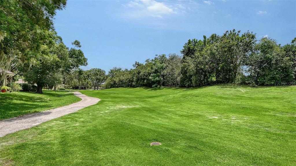 A paved path winds through a grassy lawn bordered by trees under a blue sky — 4004 PENSHURST PARK, SARASOTA, FL
