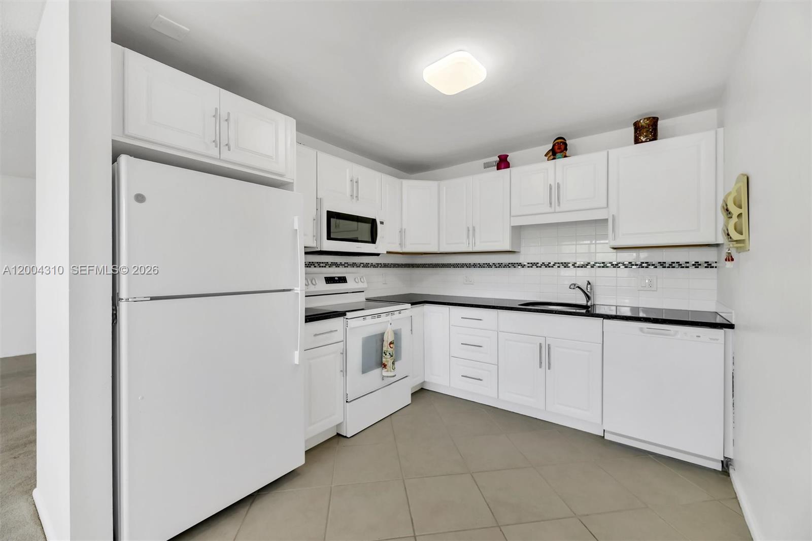 A kitchen features white cabinets, black countertops, white appliances, and light-colored tile flooring — 3013 Ventnor G # 3, Deerfield Beach FL 33442, DEERFIELD BEACH, FL