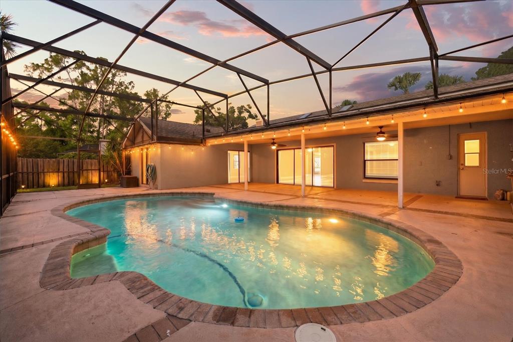 A swimming pool with a brick border sits inside a screened-in patio at dusk — 478 SABAL TRAIL CIRCLE, LONGWOOD, FL