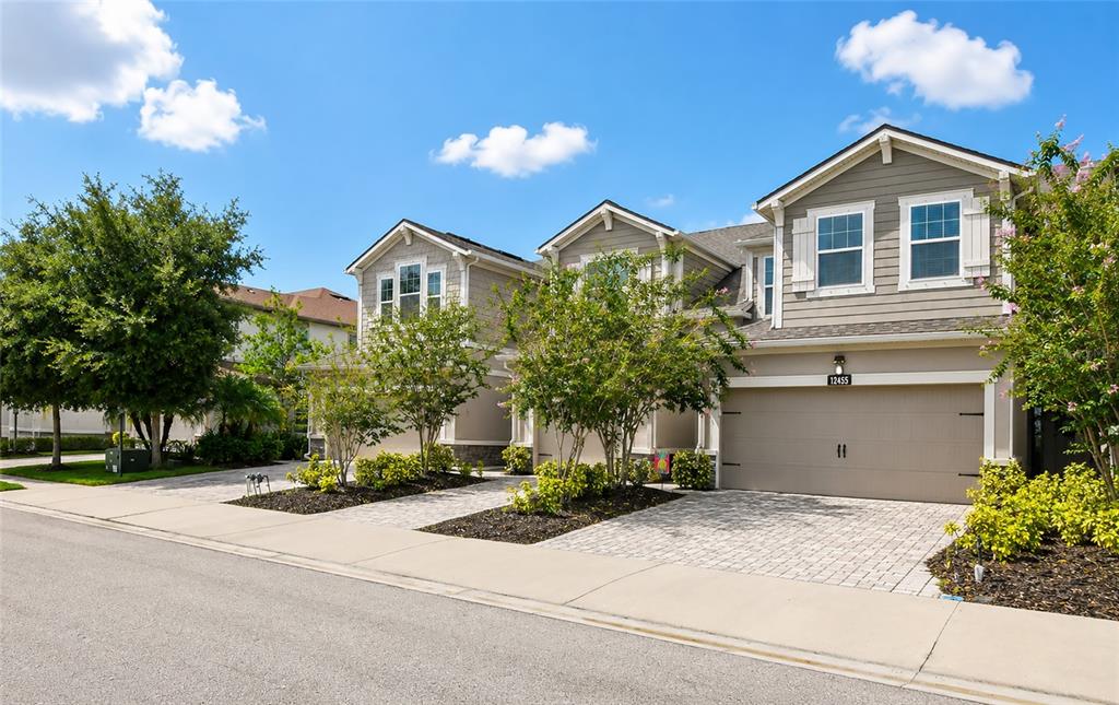 A row of two-story townhouses with beige siding, attached garages, and paved driveways under blue skies — 12455 TRAILHEAD DRIVE, BRADENTON, FL