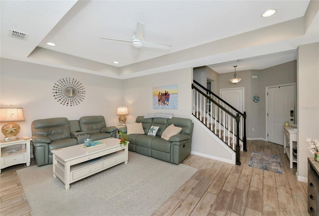 A living room features a tray ceiling, light-colored tile flooring, and two green leather sofas — 12455 TRAILHEAD DRIVE, BRADENTON, FL
