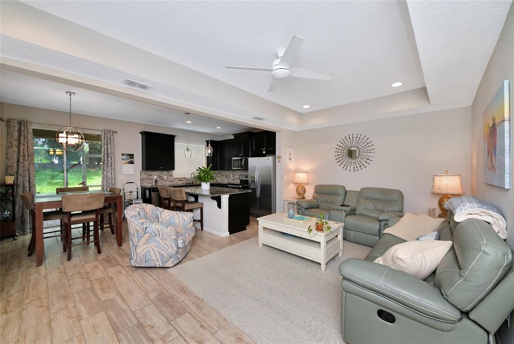 An open-concept living room and kitchen featuring light tile floors, grey leather furniture, and cabinetry — 12455 TRAILHEAD DRIVE, BRADENTON, FL