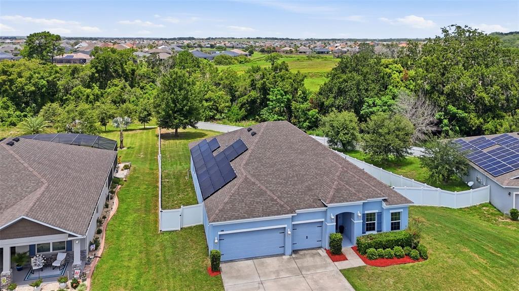 An aerial view shows a blue house with solar panels on its roof and a yard — 1948 BELL CREEK LOOP, FRUITLAND PARK, FL