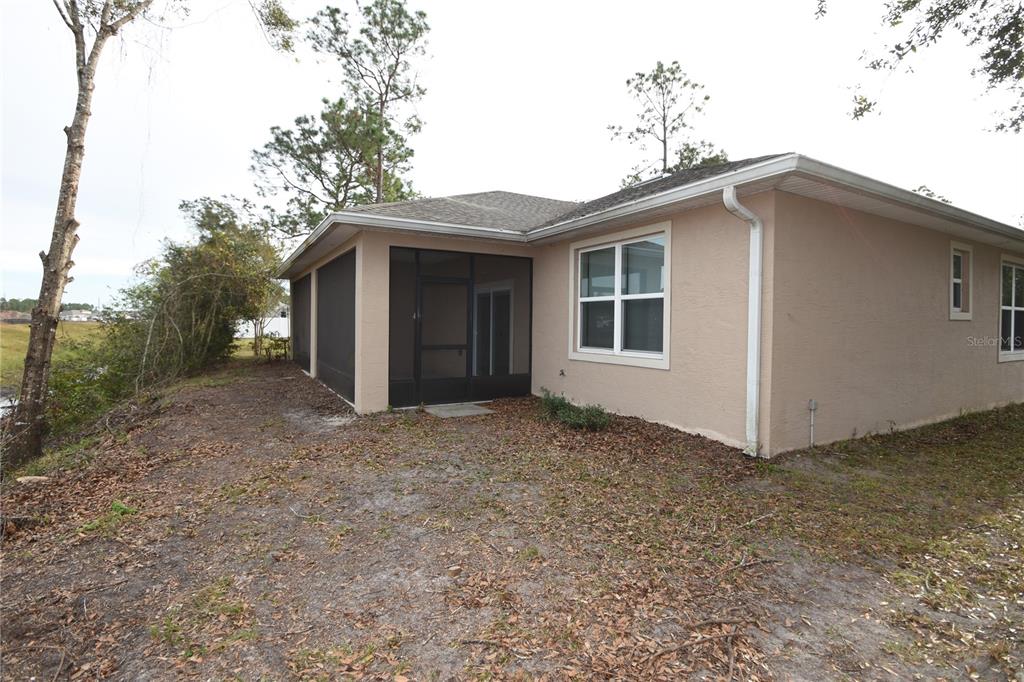 The exterior of a tan house features a screened-in porch and a grassy backyard — 43 LLOYD TRAIL, PALM COAST, FL