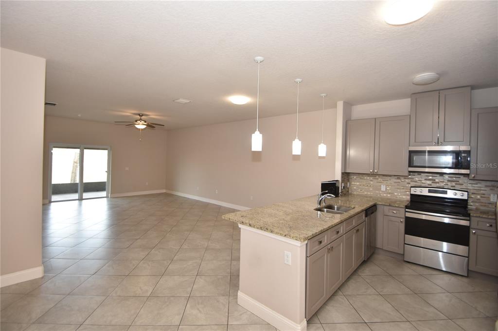 A kitchen with granite countertops and gray cabinets opens into a large tiled living area — 43 LLOYD TRAIL, PALM COAST, FL