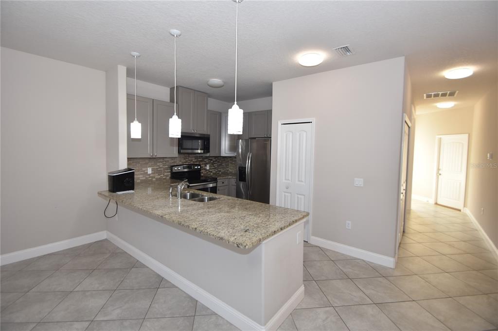 A kitchen features granite countertops, gray cabinets, stainless steel appliances, and tile flooring — 43 LLOYD TRAIL, PALM COAST, FL