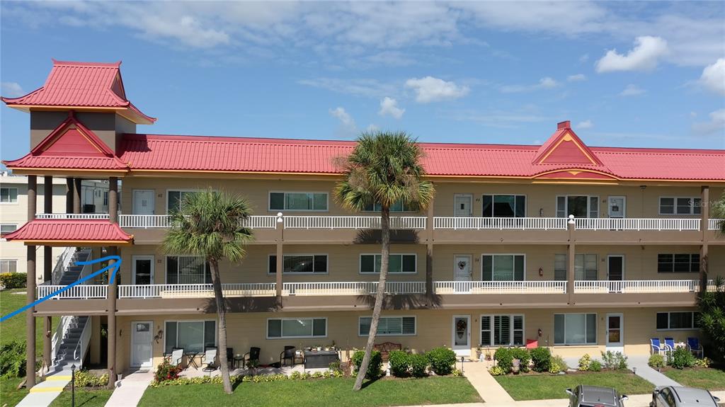 A three-story apartment building features a red metal roof and a distinctive Asian-inspired tower — 2402 ECUADORIAN WAY UNIT 22, CLEARWATER, FL