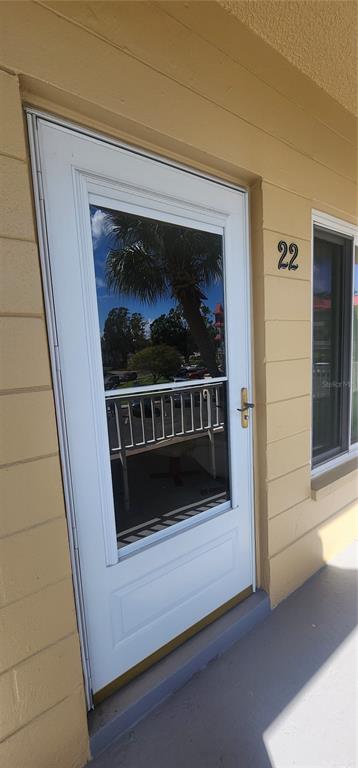 A white storm door with a glass panel is mounted on a tan exterior wall — 2402 ECUADORIAN WAY UNIT 22, CLEARWATER, FL