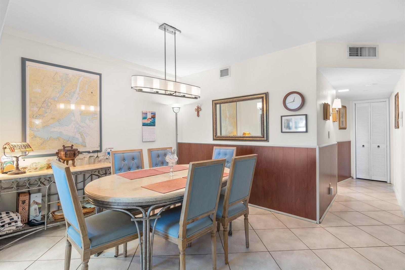 A dining room features a wooden table with blue chairs, wood wainscoting, and tile flooring — 100 SE 6th Avenue # 304, Pompano Beach FL 33060, POMPANO BEACH, FL