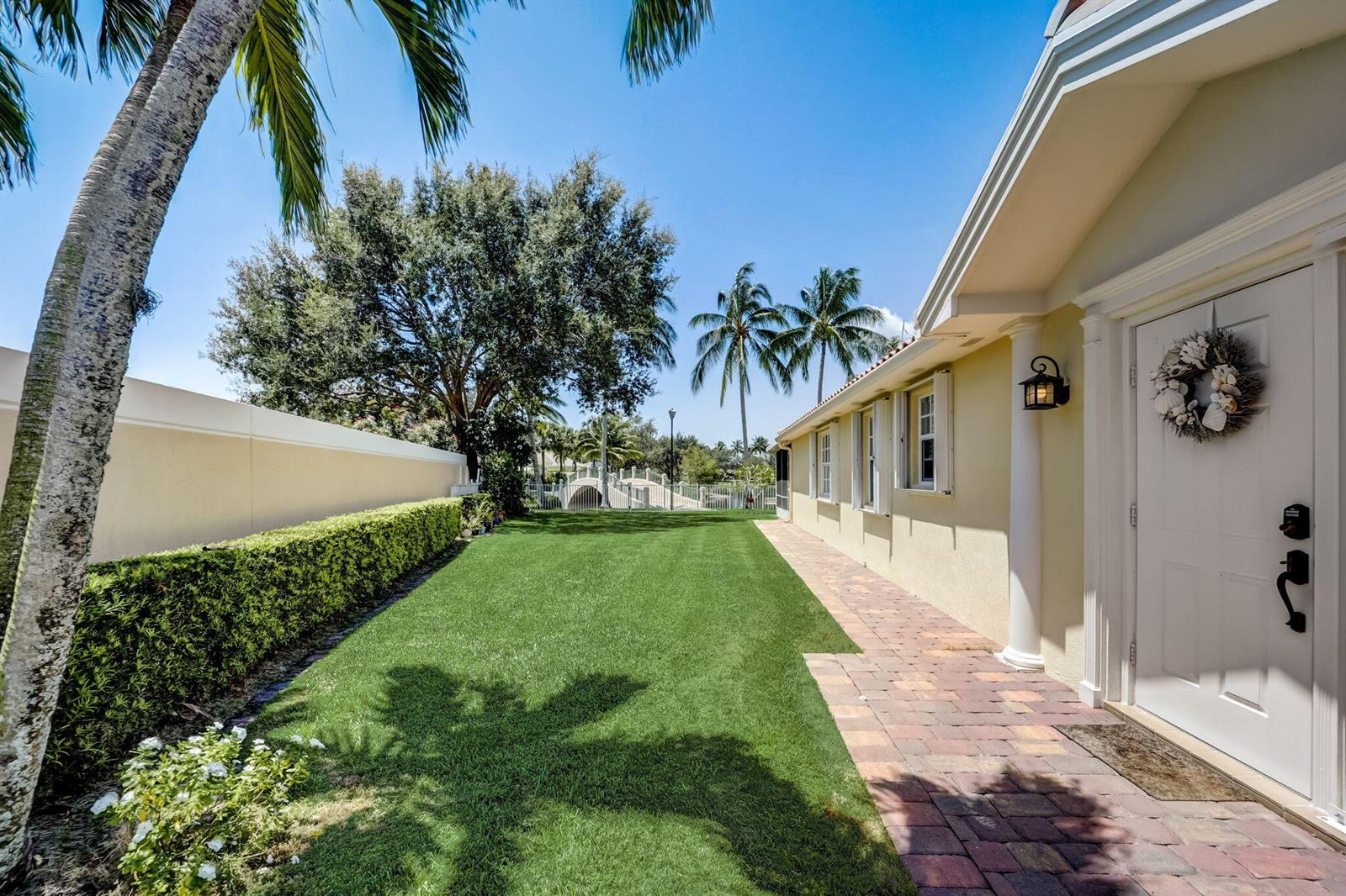 A side yard features a brick walkway, a manicured lawn, and a tall privacy hedge — 8178 Montserrat Place, Wellington FL 33414, WELLINGTON, FL