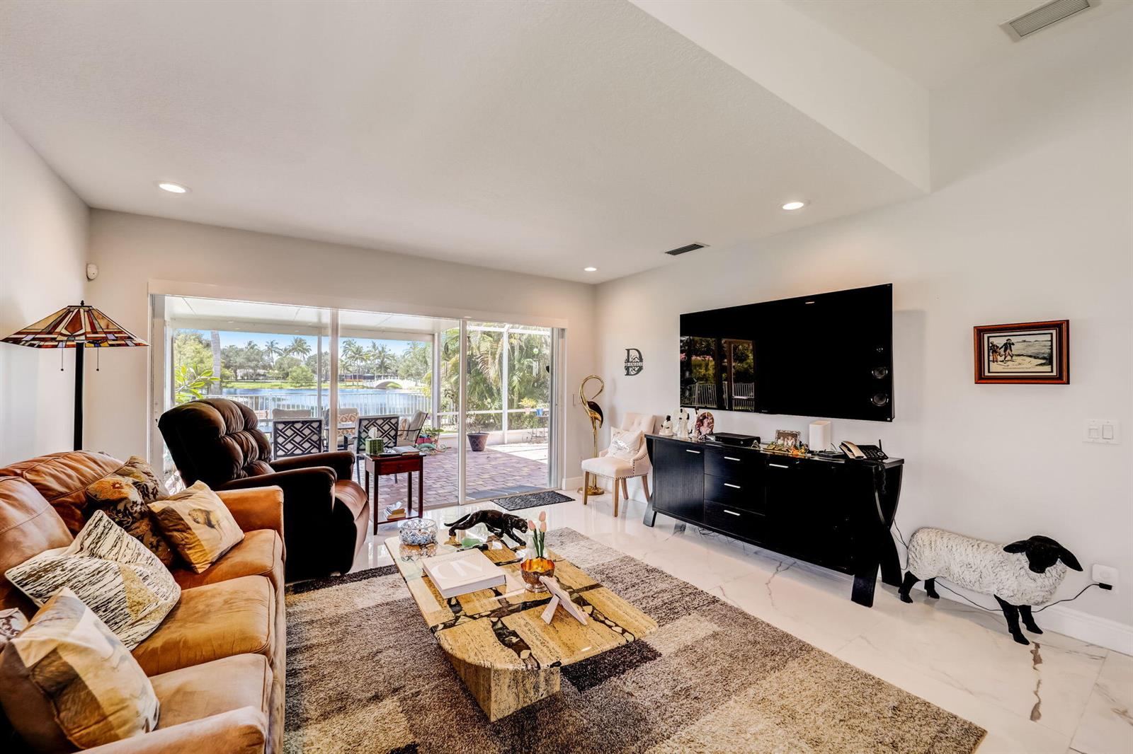 A living room features a large television, a stone coffee table, and sliding glass doors — 8178 Montserrat Place, Wellington FL 33414, WELLINGTON, FL