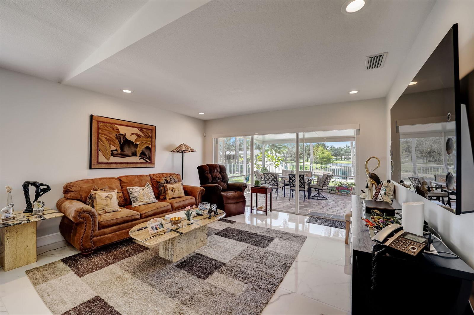 A living room with a brown sofa, patterned rug, and sliding doors opening to a patio — 8178 Montserrat Place, Wellington FL 33414, WELLINGTON, FL