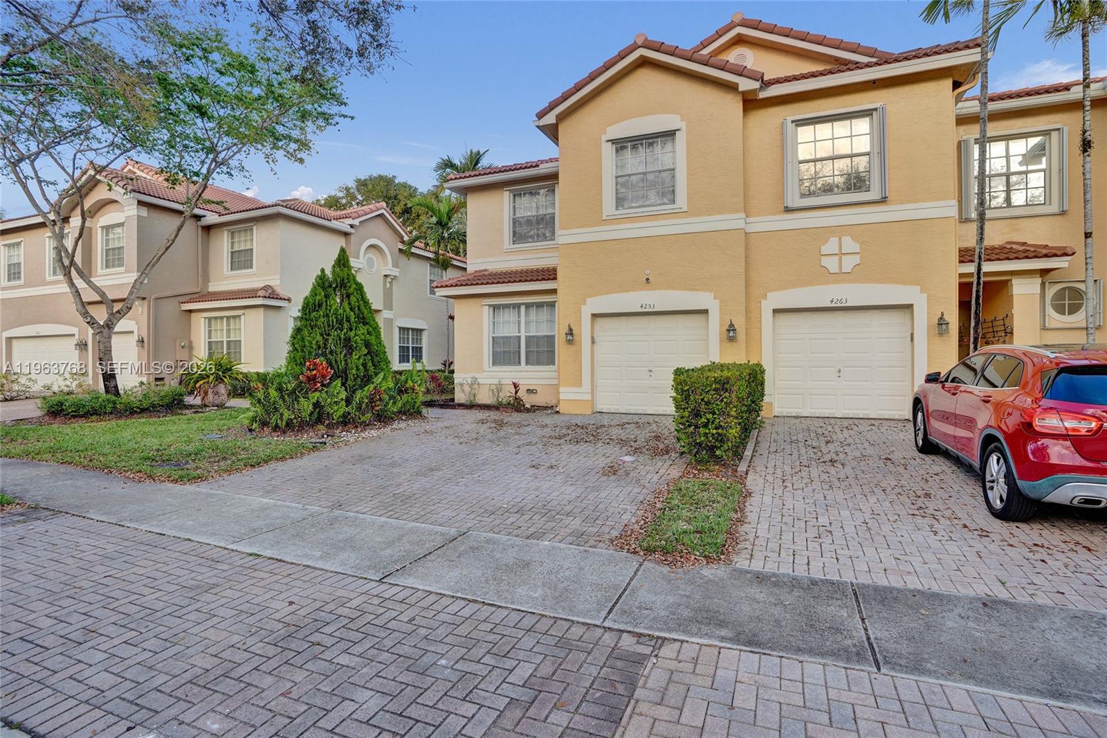 A two-story yellow stucco townhouse with a paved driveway and a red car parked outside — 4253 SW 124th Ter, Miramar FL 33027, MIRAMAR, FL