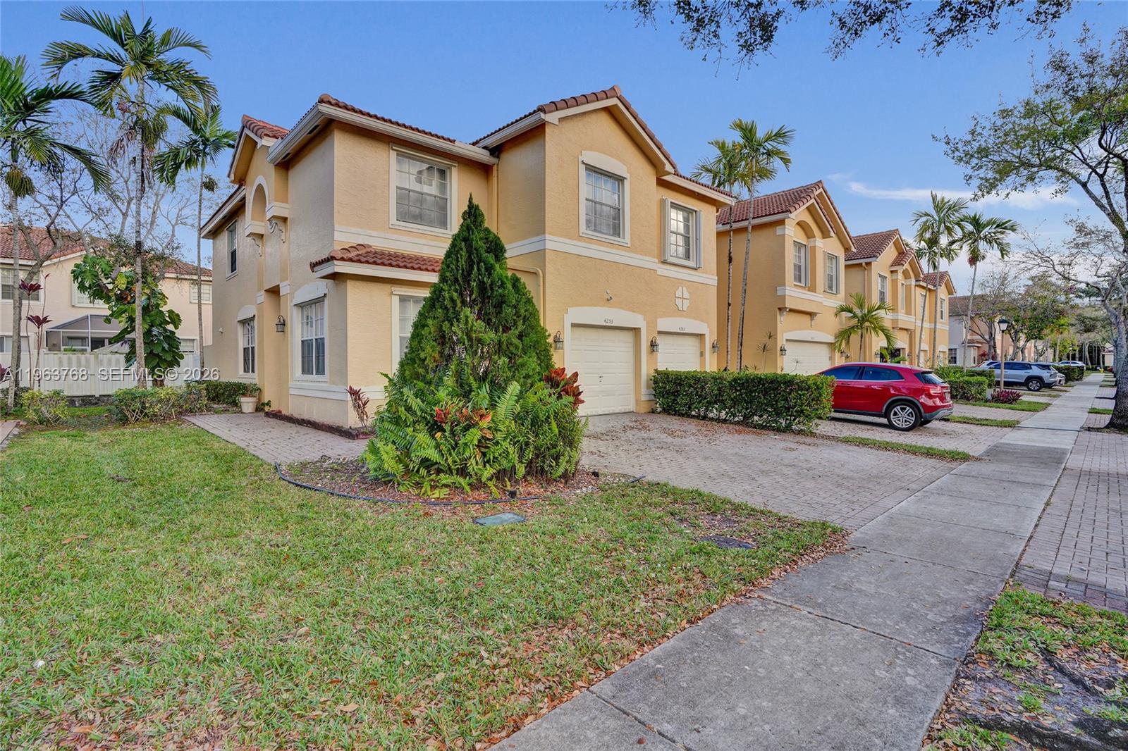 A two-story yellow stucco townhouse with a paved driveway and a red car parked outside — 4253 SW 124th Ter, Miramar FL 33027, MIRAMAR, FL