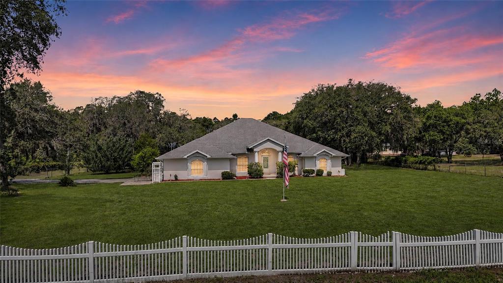 A single-story house with a white fence stands on a large lawn at sunset — 5260 SW 176TH AVENUE, DUNNELLON, FL