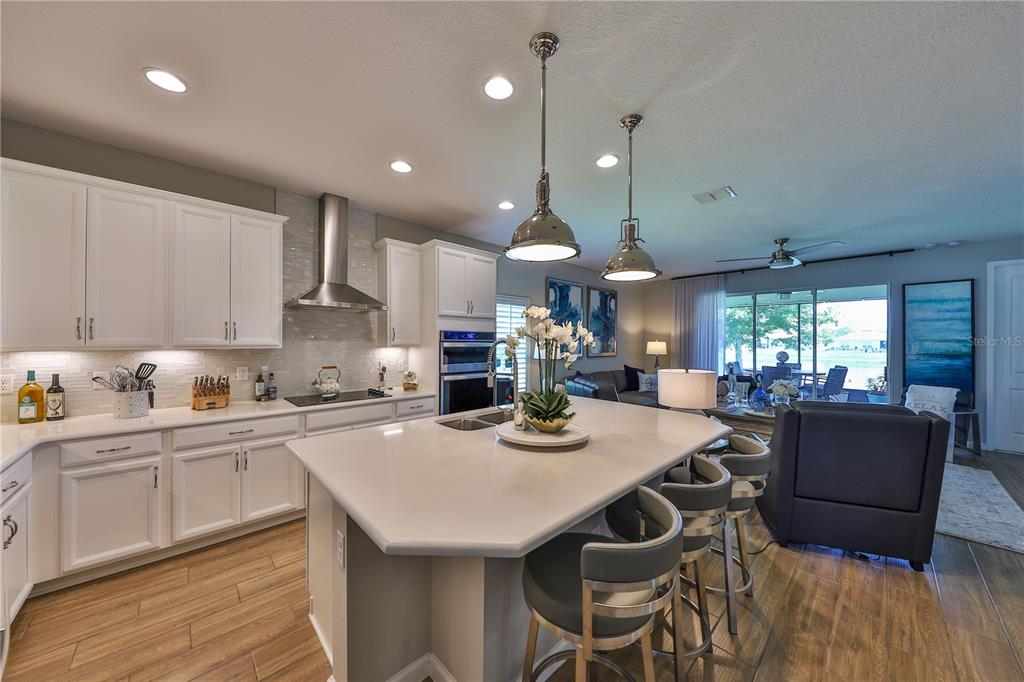 A modern kitchen features white cabinetry, a large quartz island, and stainless steel appliances — 1049 WANDERER DRIVE, DELTONA, FL