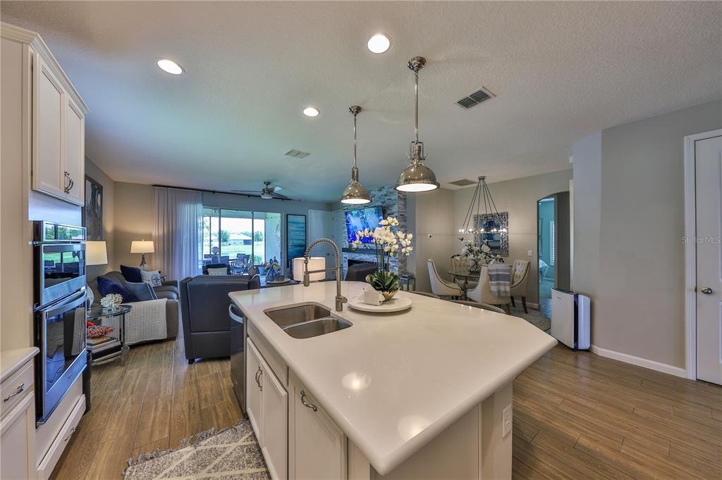 A kitchen island with a double sink sits in an open-concept home with wood flooring — 1049 WANDERER DRIVE, DELTONA, FL