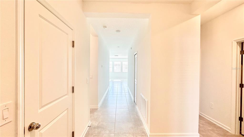 A bright hallway with white walls and light-colored tile flooring leads toward a windowed room — 683 DARING DRIVE, DAVENPORT, FL