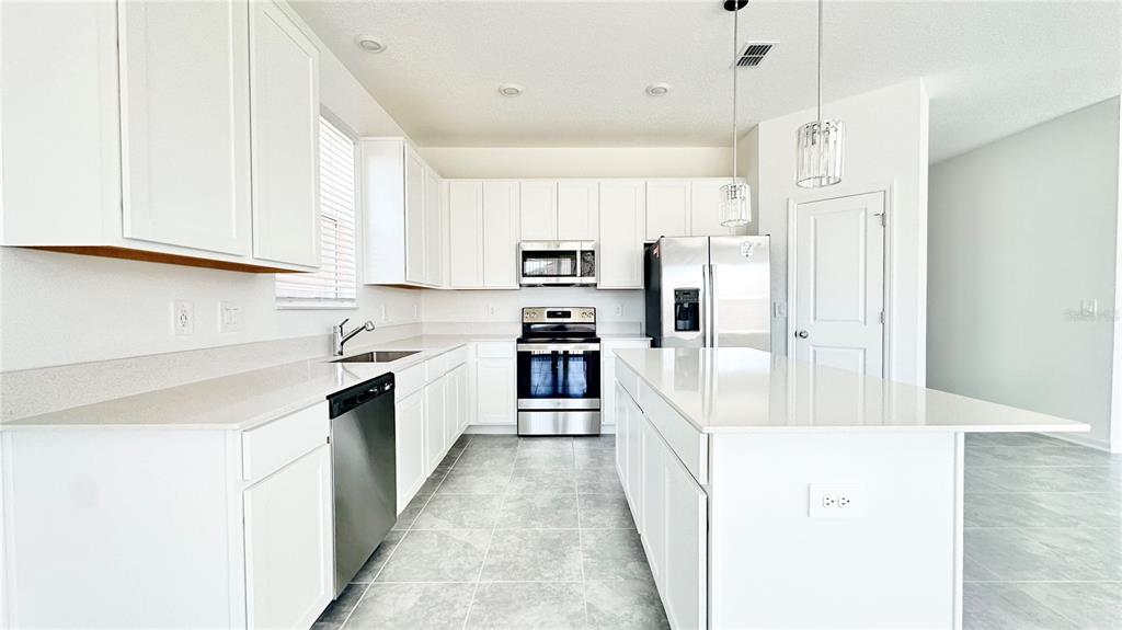A modern kitchen features white cabinets, stainless steel appliances, a center island, and tile flooring — 683 DARING DRIVE, DAVENPORT, FL