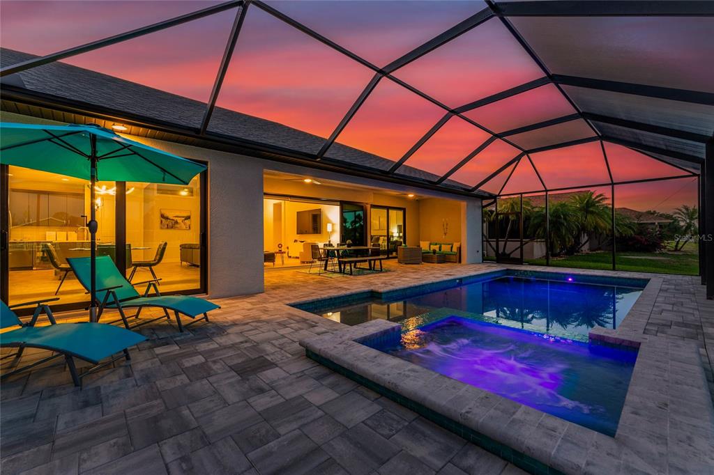A screened-in patio features a pool, a hot tub, and lounge chairs at sunset — 35 MEDALIST COURT, ROTONDA WEST, FL