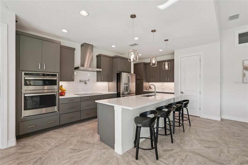 A modern kitchen features gray cabinets, stainless steel appliances, a white island, and tile flooring — 35 MEDALIST COURT, ROTONDA WEST, FL