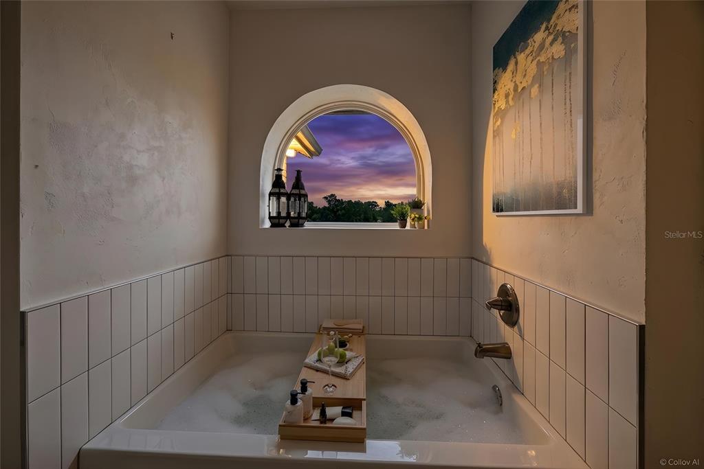 A bathtub with a wooden tray sits beneath an arched window overlooking a sunset sky — 10240 NW 7TH TERRACE, BRANFORD, FL