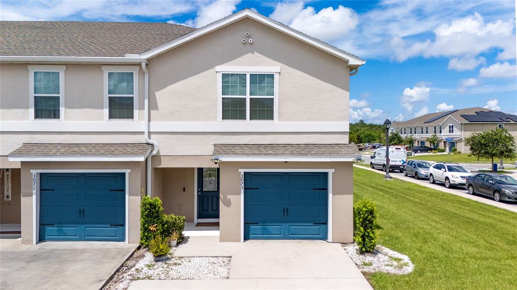 An exterior view of a two-story townhouse with blue garage doors and a concrete driveway — 3075 FIELDWOOD CIRCLE, ST CLOUD, FL