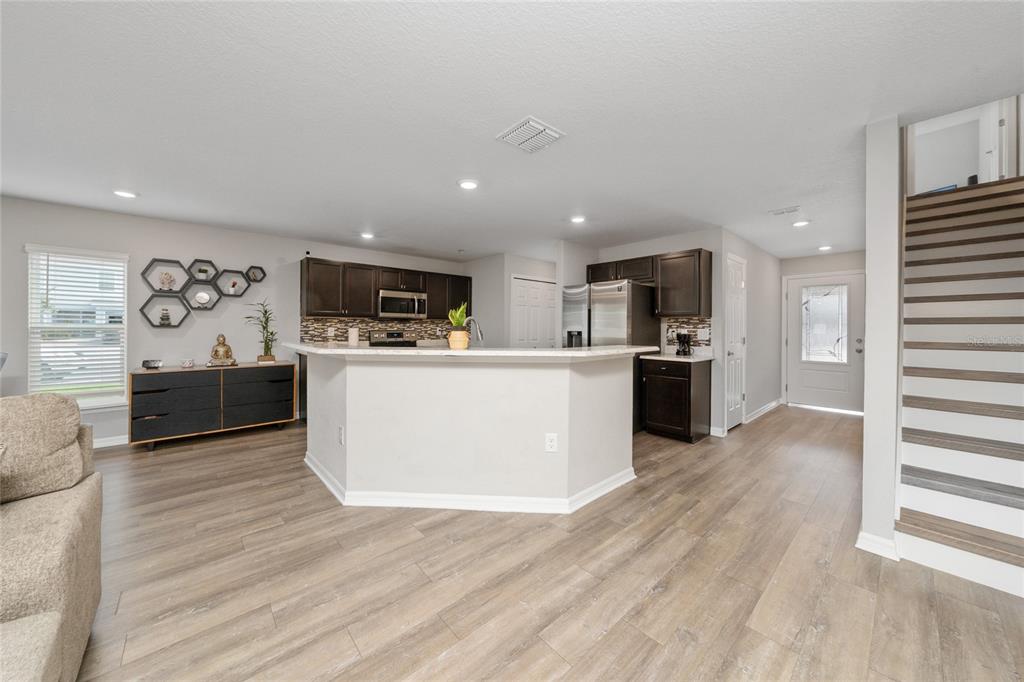 An open-concept kitchen features dark wood cabinets, a breakfast bar, and light wood-look flooring — 3075 FIELDWOOD CIRCLE, ST CLOUD, FL