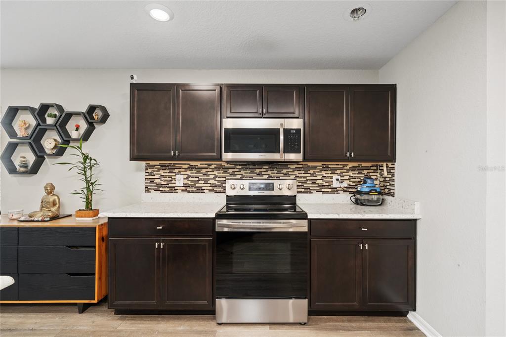 A kitchen features dark wood cabinets, stainless steel appliances, and a mosaic tile backsplash — 3075 FIELDWOOD CIRCLE, ST CLOUD, FL