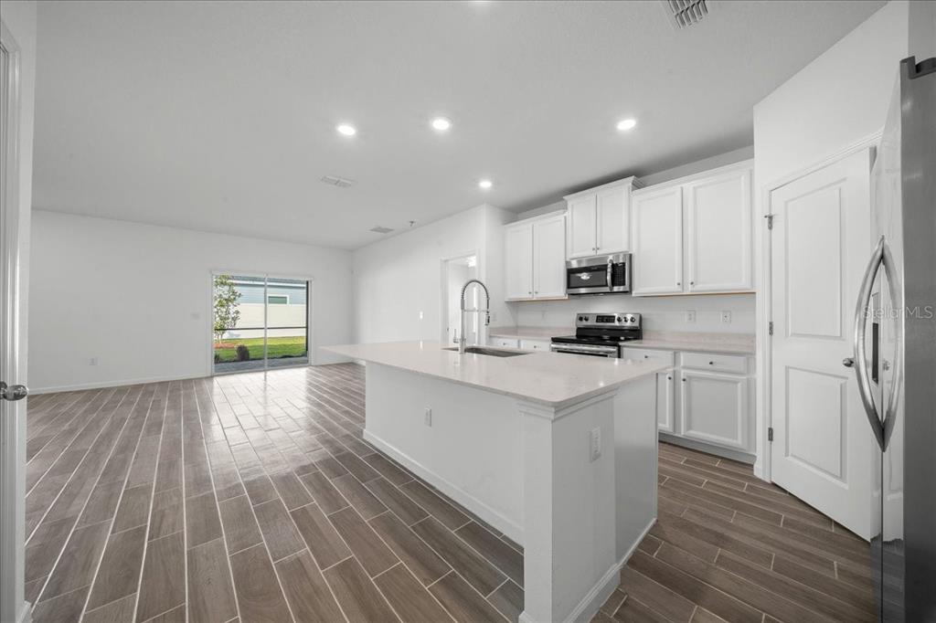 A modern kitchen features white cabinetry, a central island, and wood-look tile flooring — 7542 SW 76TH TERRACE, OCALA, FL
