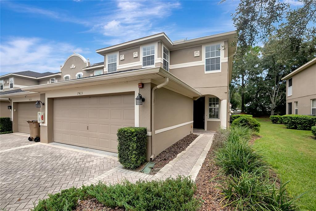 A two-story townhouse exterior with a tan stucco facade, a two-car garage, and paved driveway — 7413 TERRACE RIVER DRIVE, TEMPLE TERRACE, FL