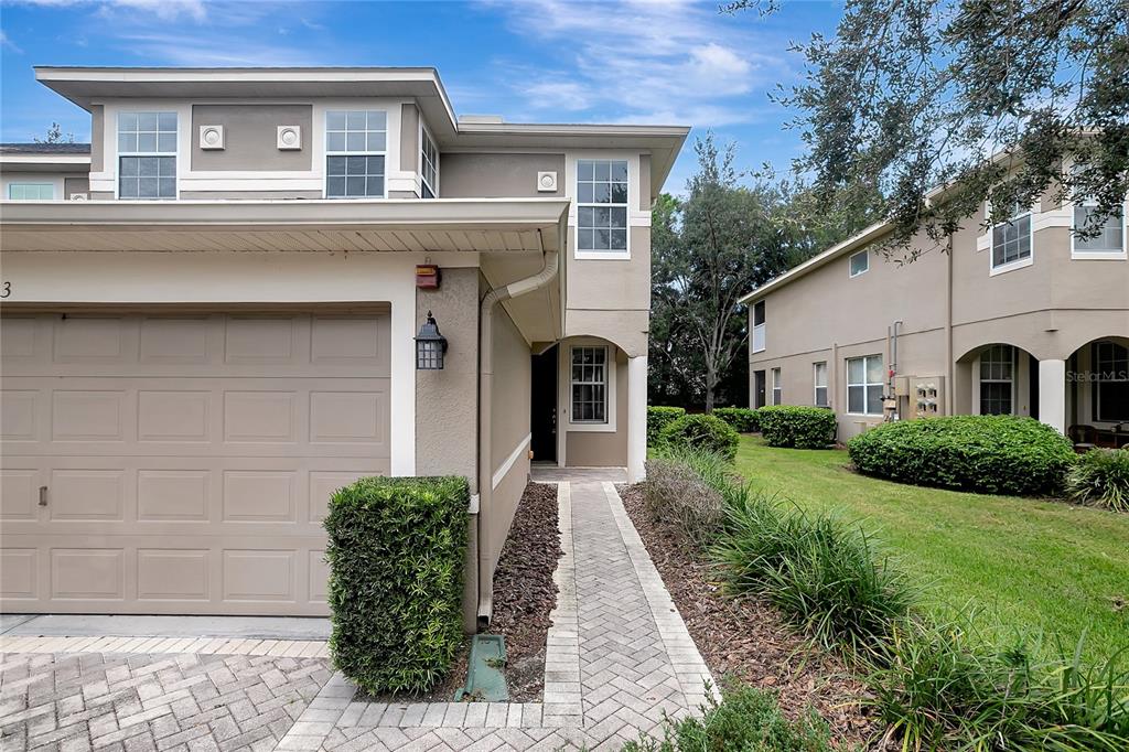 A two-story townhouse exterior features a beige facade, a garage, and a paved walkway — 7413 TERRACE RIVER DRIVE, TEMPLE TERRACE, FL