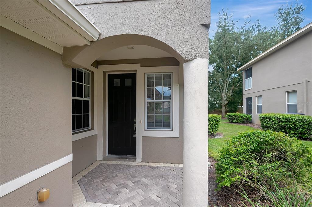 A covered entryway with a brick paver floor, a black front door, and a stucco exterior — 7413 TERRACE RIVER DRIVE, TEMPLE TERRACE, FL