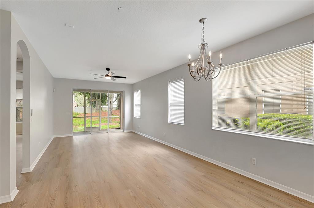A bright, empty living room with light wood-look flooring, a chandelier, and a ceiling fan — 7413 TERRACE RIVER DRIVE, TEMPLE TERRACE, FL