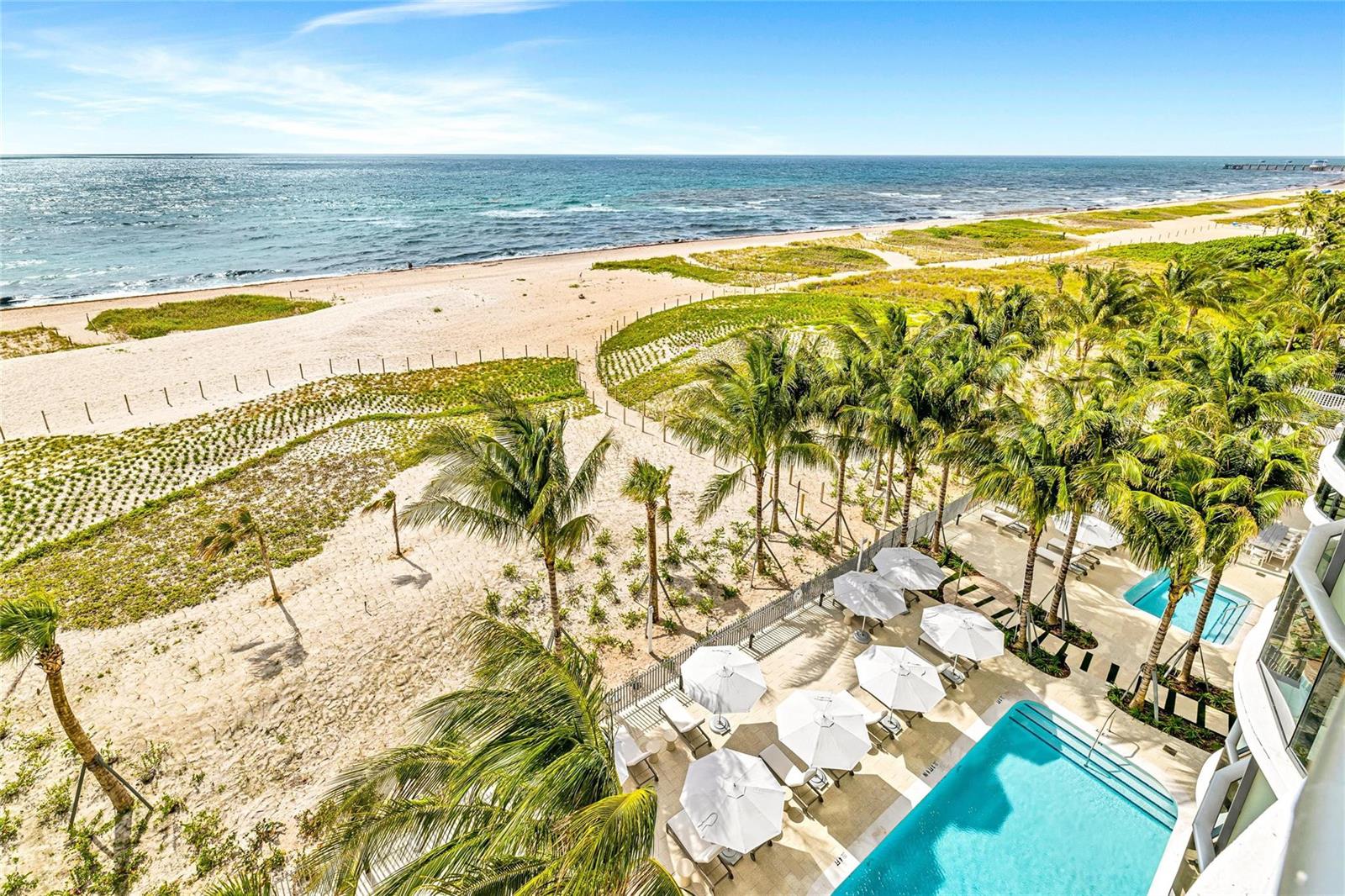 An aerial view shows a swimming pool with white umbrellas next to a sandy beach — 900 N Ocean Boulevard # 606, Pompano Beach FL 33062, POMPANO BEACH, FL