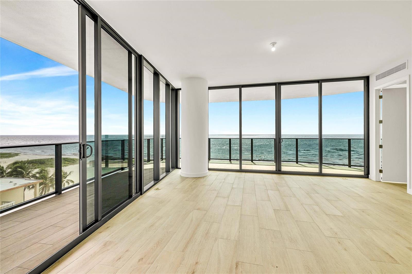 An empty room with light wood-look flooring features floor-to-ceiling windows overlooking the ocean — 900 N Ocean Boulevard # 606, Pompano Beach FL 33062, POMPANO BEACH, FL