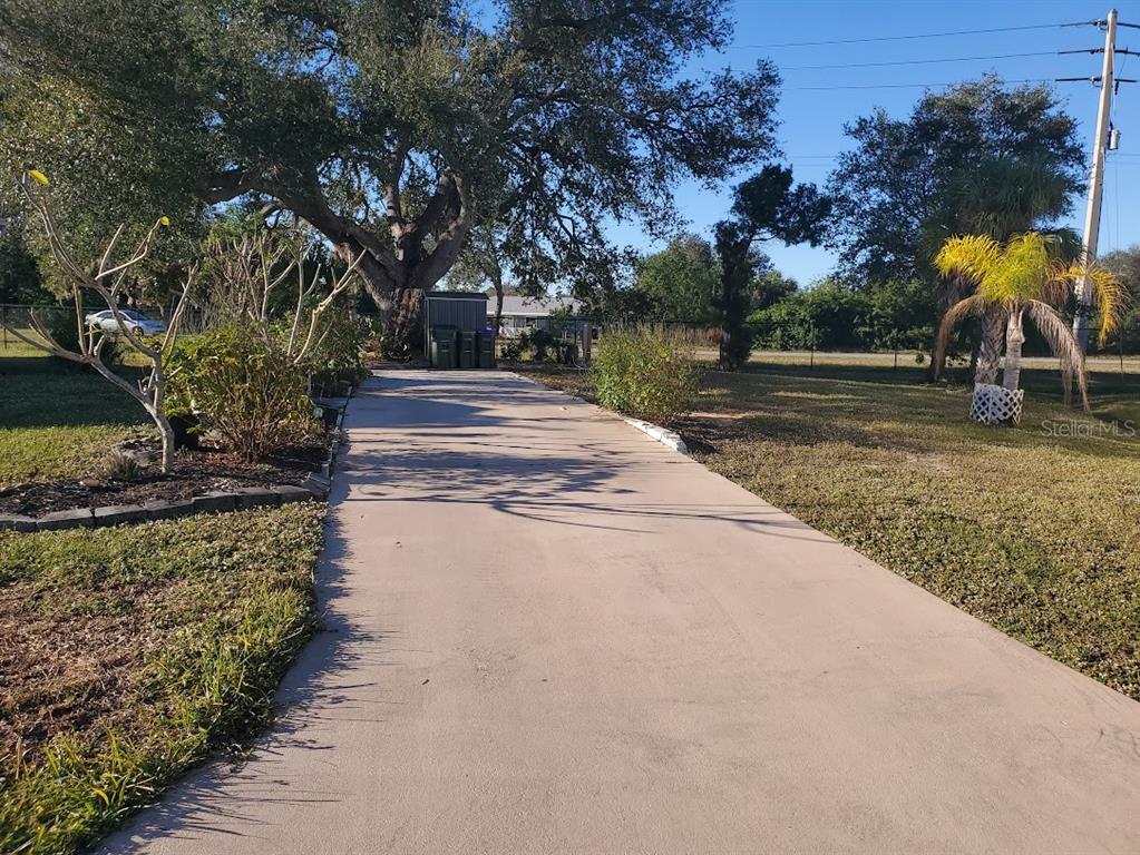 A concrete driveway leads toward a small shed on a grassy lot with trees — 6880 PLEASANT COURT, NORTH PORT, FL