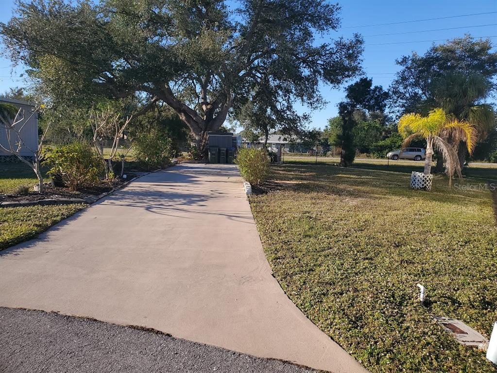 A concrete driveway leads toward a large tree and a shed in a grassy yard — 6880 PLEASANT COURT, NORTH PORT, FL