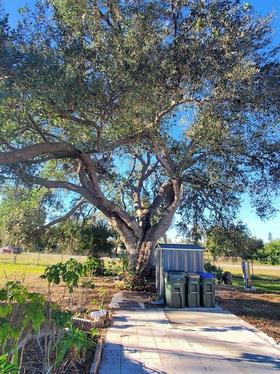 A large, mature oak tree stands over a paved patio with three outdoor trash bins — 6880 PLEASANT COURT, NORTH PORT, FL