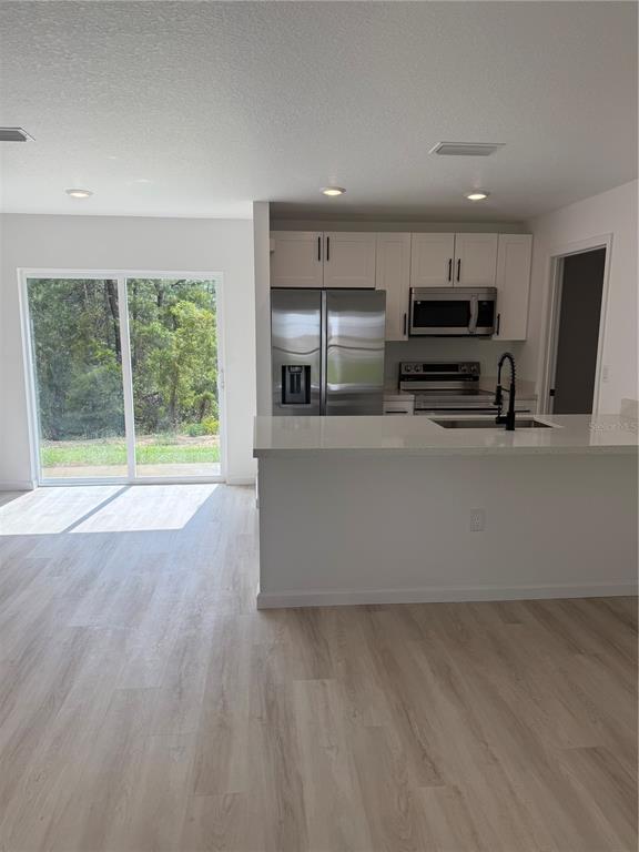 A kitchen with white cabinets, stainless steel appliances, and a breakfast bar overlooks a backyard — 12854 SW 84TH TERRACE ROAD, OCALA, FL